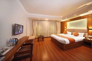 A hotel room with a wooden bed, a TV on the wall, a desk with a chair, and a small table with a plant. - Hotel Mums Home (Kathmandu)