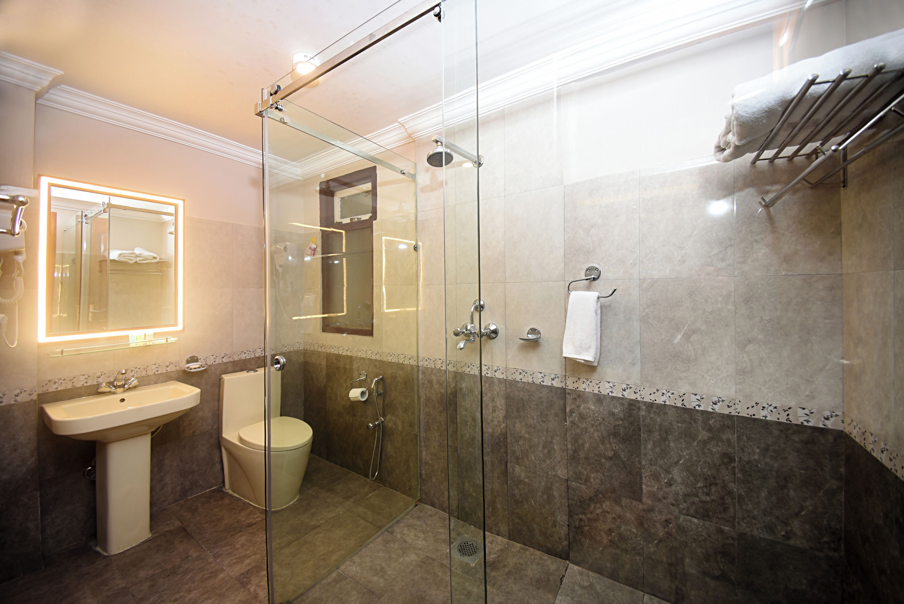 Un baño moderno con ducha de vidrio, lavamanos pedestal y retrete.
