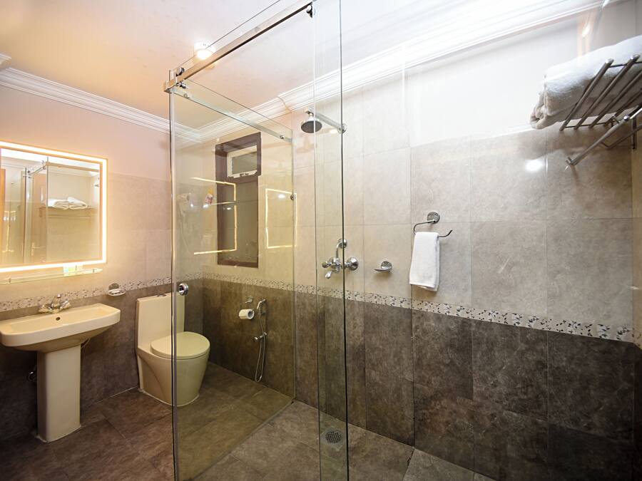 Un baño moderno con ducha de vidrio, lavamanos pedestal y retrete.