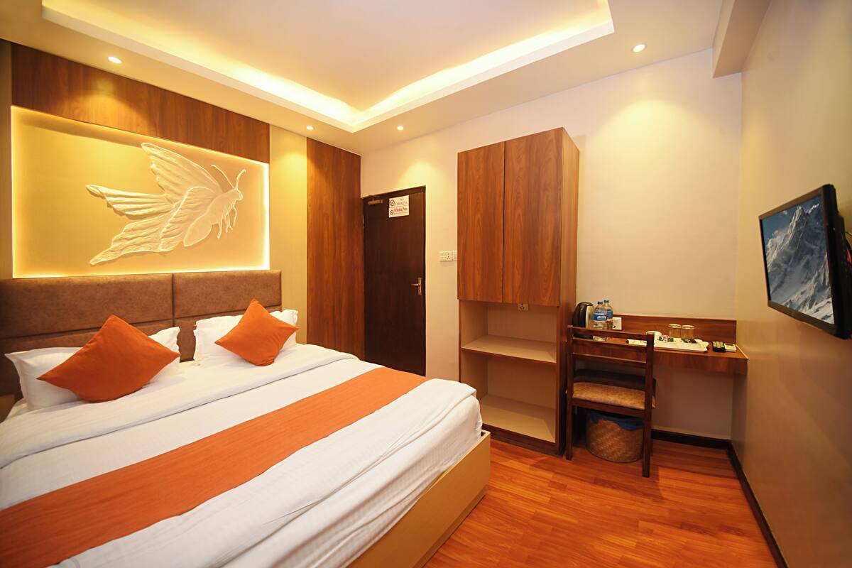 Een hotelkamer met een groot bed, een houten hoofdbord en een wandlamp met een vleugelmotief.