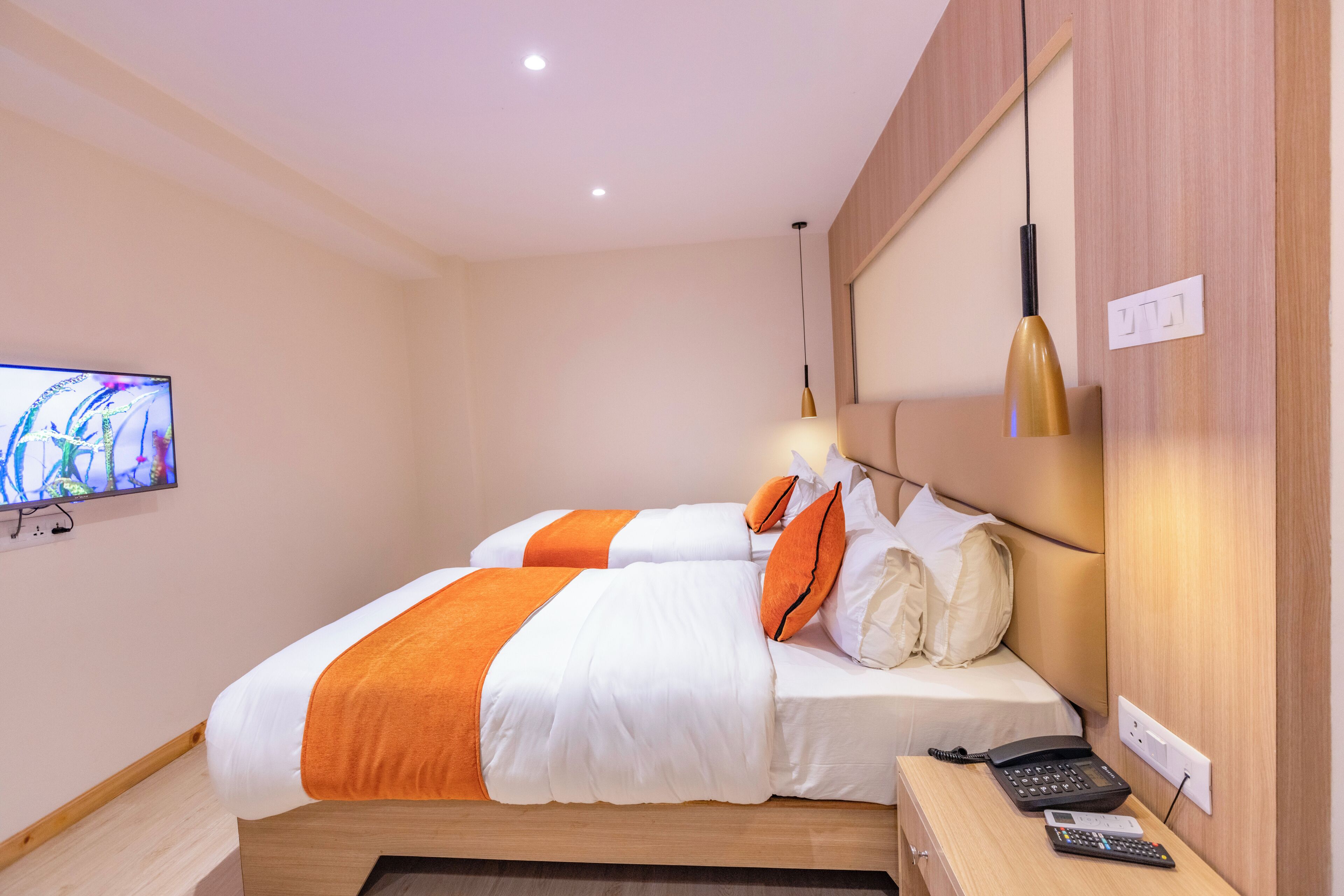 Habitación de hotel con cama, televisor, mesita de noche con teléfono y lámpara de pared.