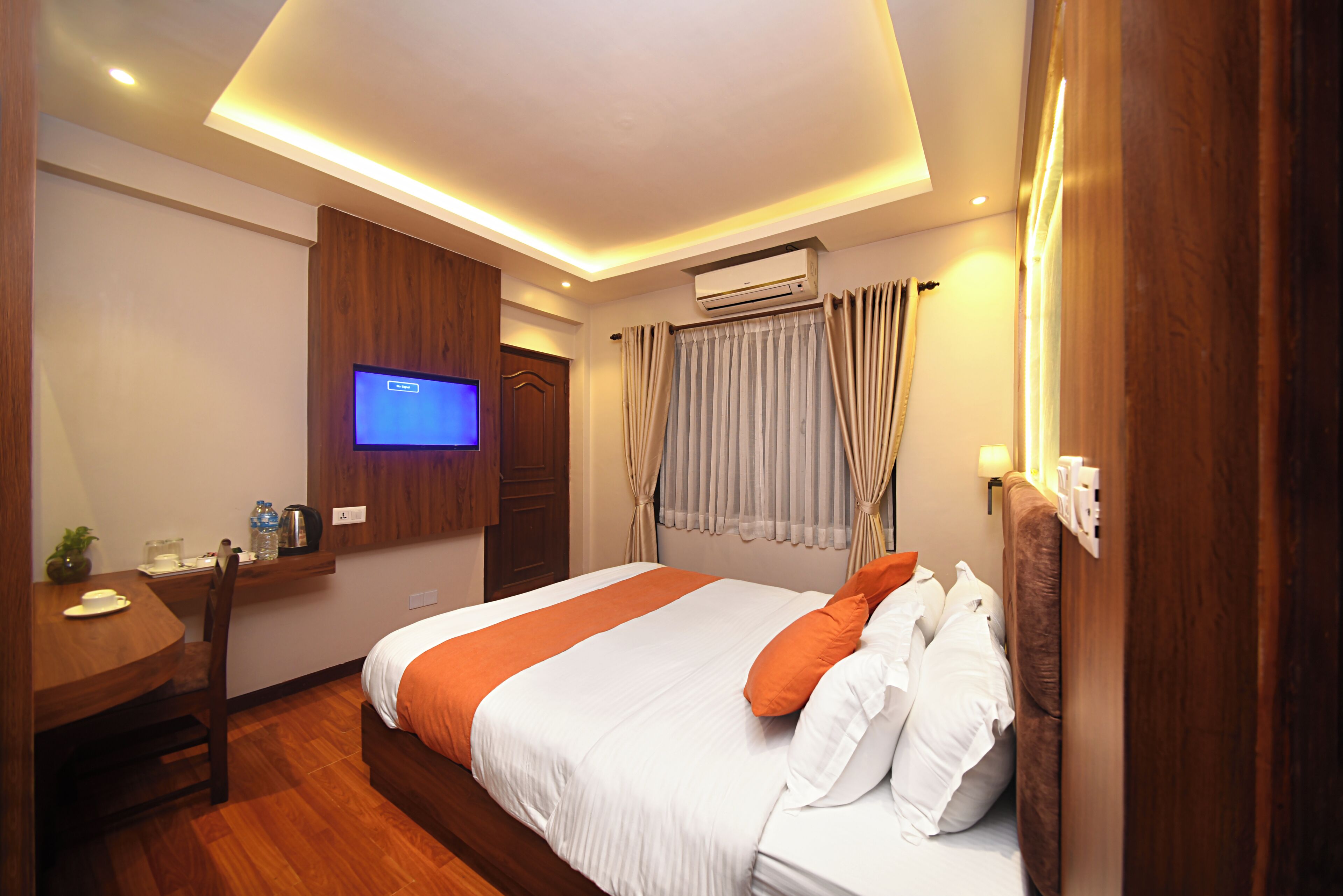Quarto de hotel com uma cama, escrivaninha, televisão e aparelho de ar condicionado.