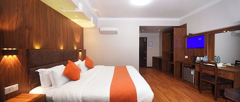 Habitación de hotel con una cama grande, cabecera de madera, mesitas de noche, un escritorio con silla, televisor y equipo de aire acondicionado.