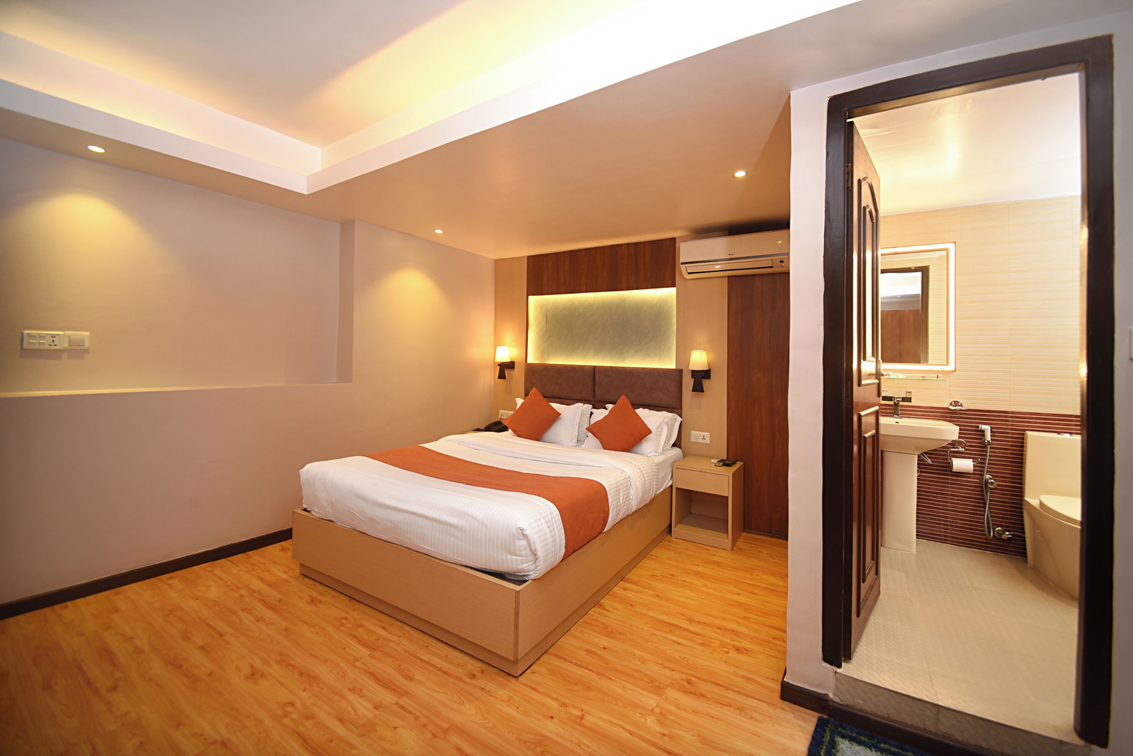 Una habitación de hotel moderna con una cama grande, mesitas de noche, un armario empotrado y un baño con lavabo e inodoro.