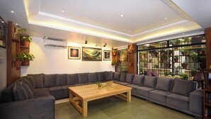 A modern living room with a sectional sofa, a wooden coffee table, and a large window with a view of greenery. - Hotel Mums Home (Kathmandu)