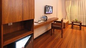 A compact hotel room with a wooden wardrobe, a small fridge, a television, a wooden desk, a chair, and a window with curtains. - Hotel Mums Home (Kathmandu)