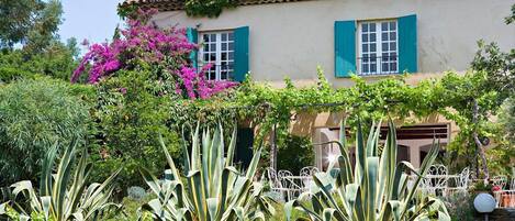 Una casa con jardín, un patio con valla de metal blanca y techo de tejas.
