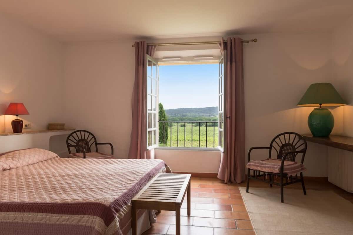 Un dormitorio con cama, ventana con vistas al campo, dos sillas y una mesa.