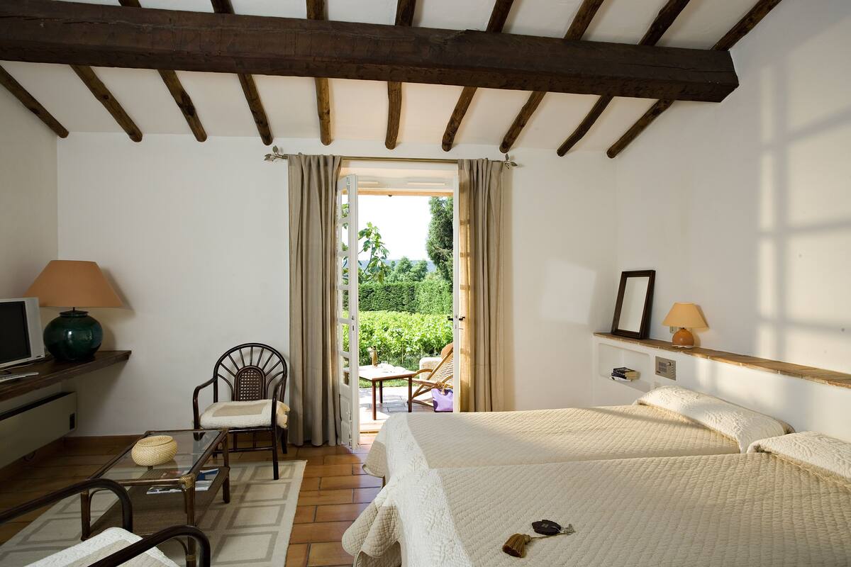 Un dormitorio con cama, una silla, una mesa, una lámpara y un televisor.