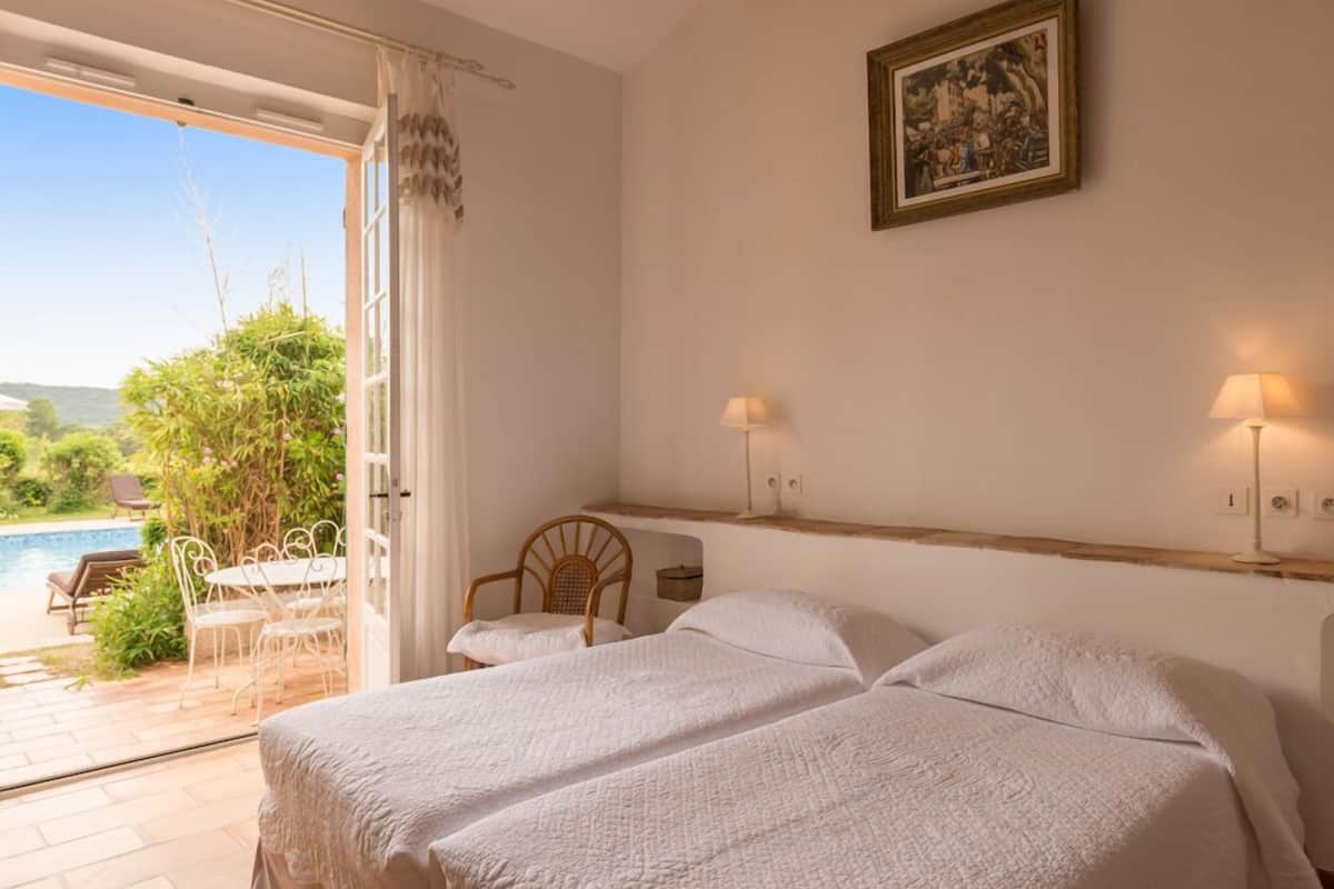 Un dormitorio con dos camas, un cabecero de madera, un cuadro en la pared y vistas a una zona de piscina al aire libre.