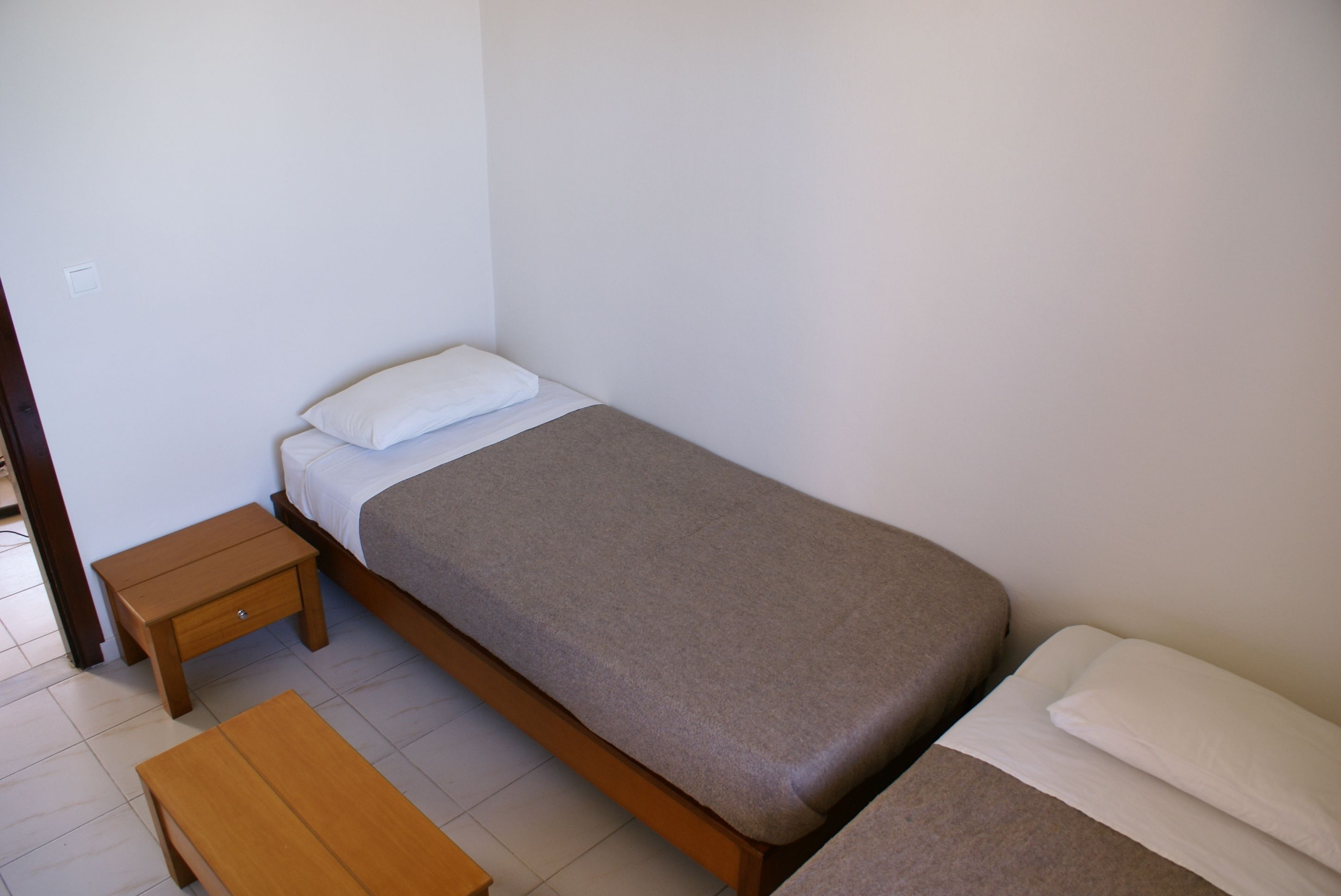 Habitació petita amb un llit individual, una nitòria de fusta i una panxa.