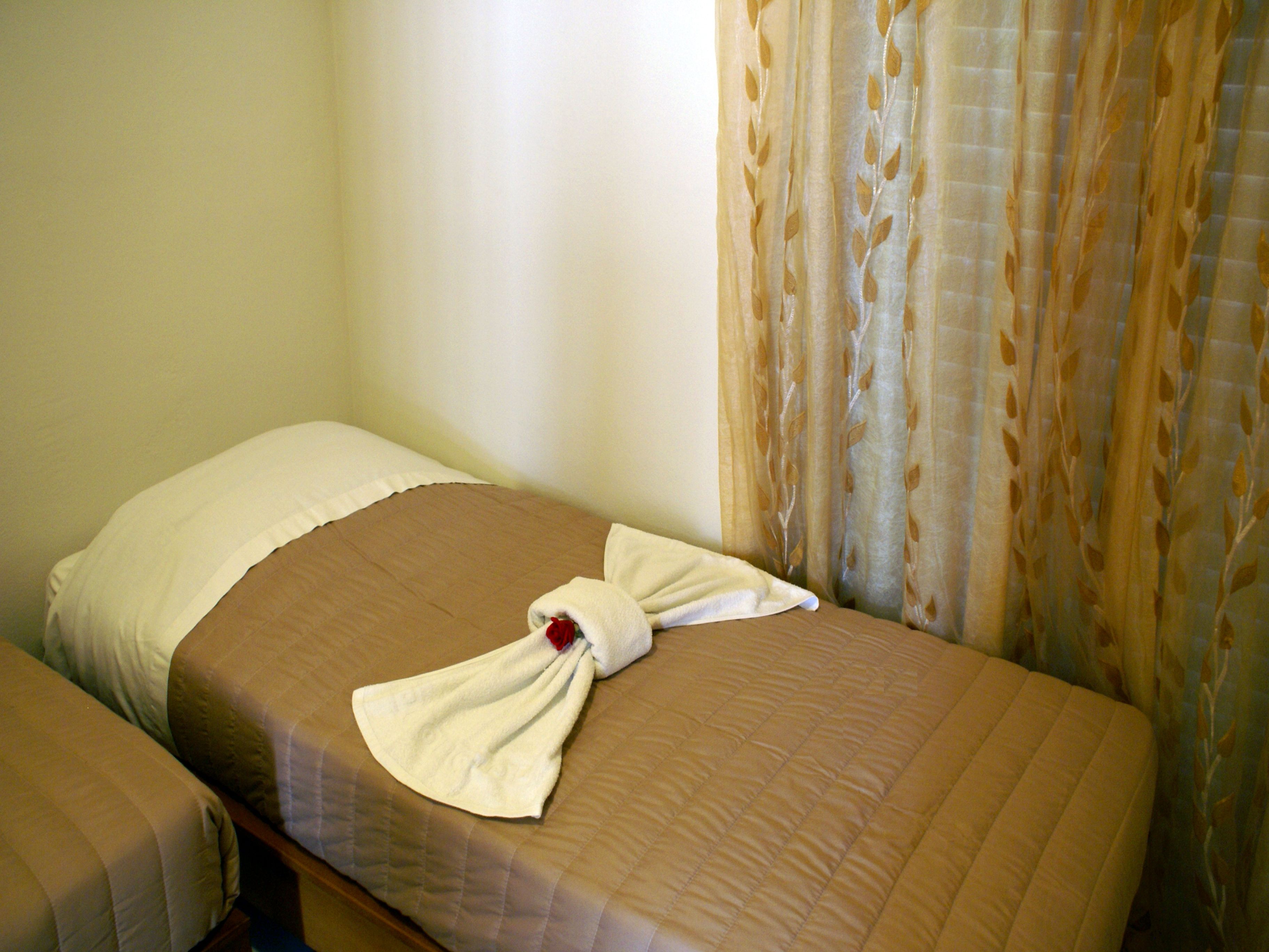 Un lit simple avec une couverture marron et un oreiller blanc. Une serviette est soigneusement pliée et posée sur le lit.