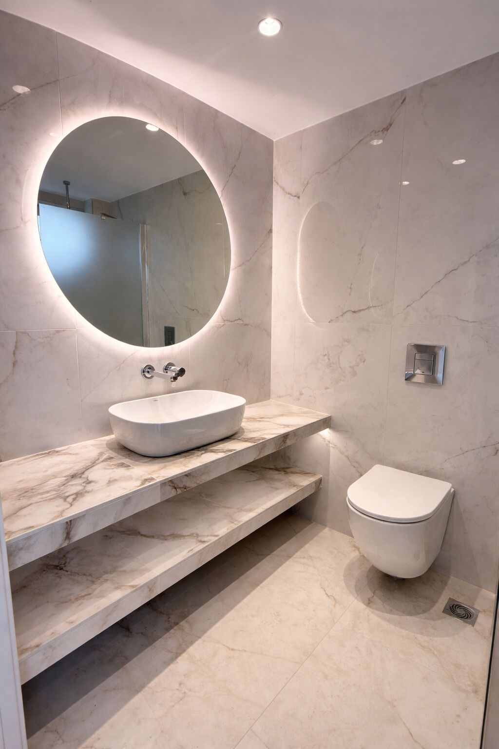 A modern bathroom with a round mirror, a vessel sink, and a toilet.