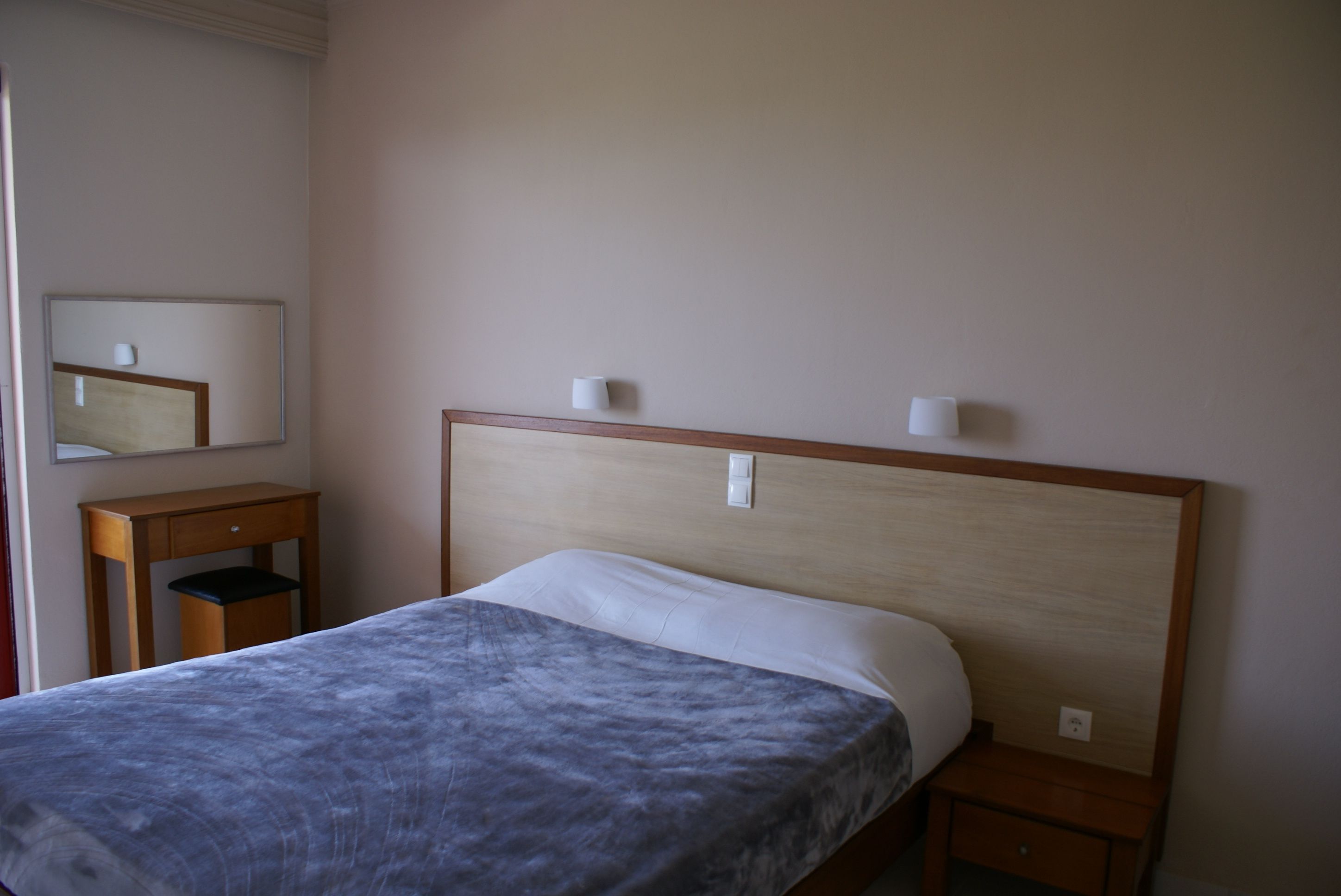 A bedroom with a bed, a nightstand, a wooden dresser, and a mirror on the wall.