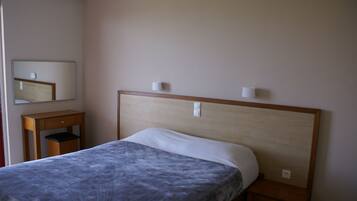 A bedroom with a bed, a nightstand, a wooden dresser, and a mirror on the wall.