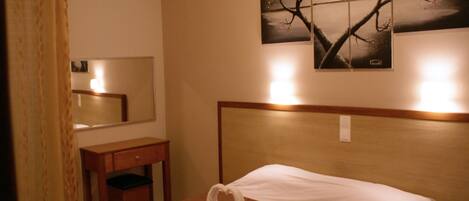 A hotel room with a bed, a nightstand, a mirror, and a wall-mounted painting of birds on a tree.