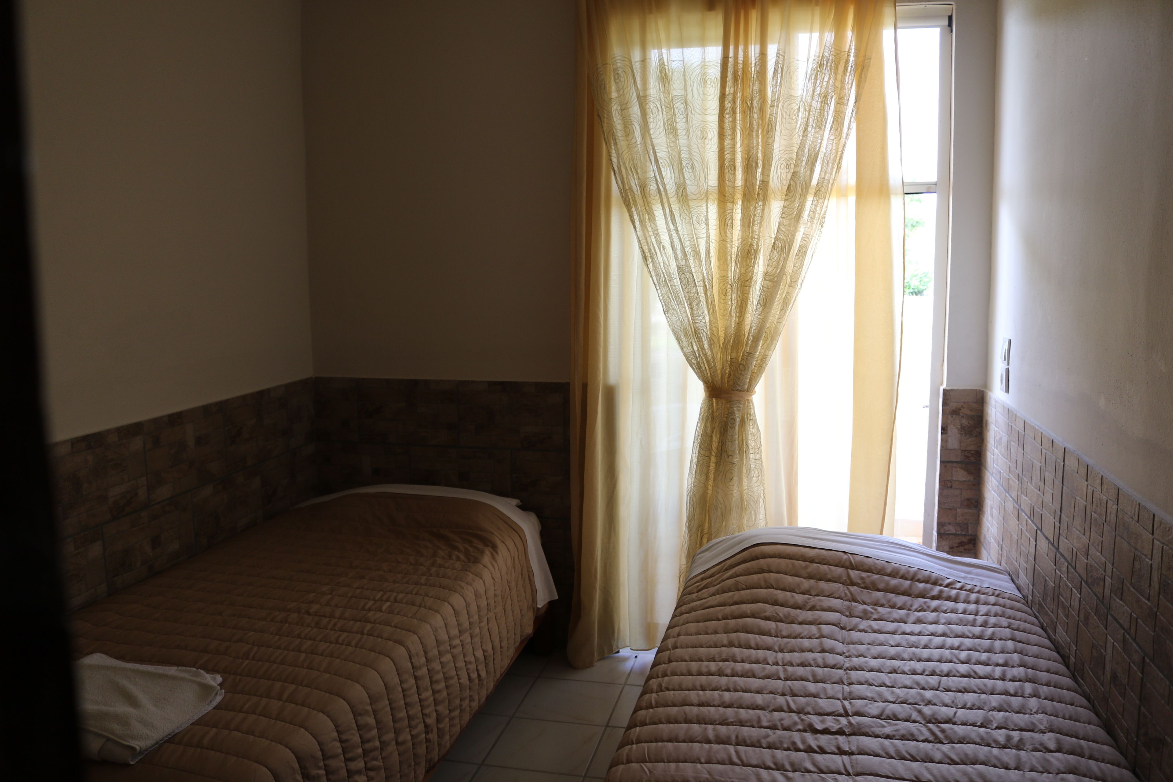 A room with two beds, a window with curtains, and a tiled floor.