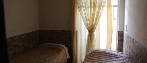 A room with two beds, a window with curtains, and a tiled floor.