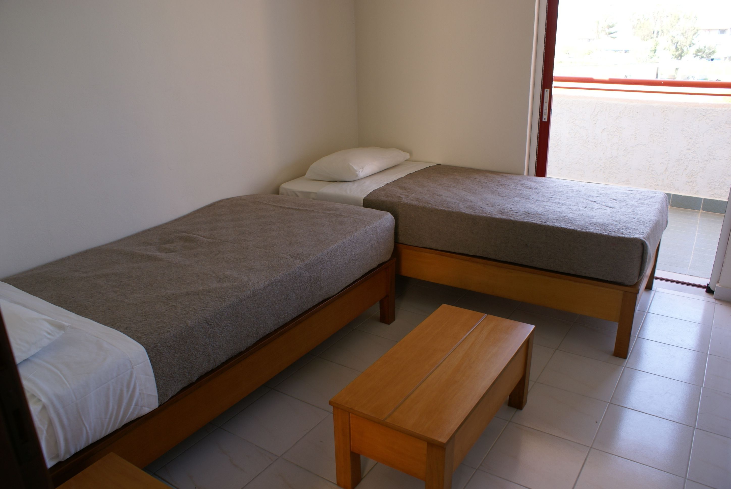 A room with two single beds, a wooden bench, and a window with a view.
