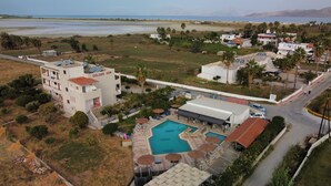 Une vue aérienne d’un complexe hôtelier avec une piscine, un bâtiment portant l’inscription « Golden Sun », et une vue sur la mer et les montagnes en arrière-plan.