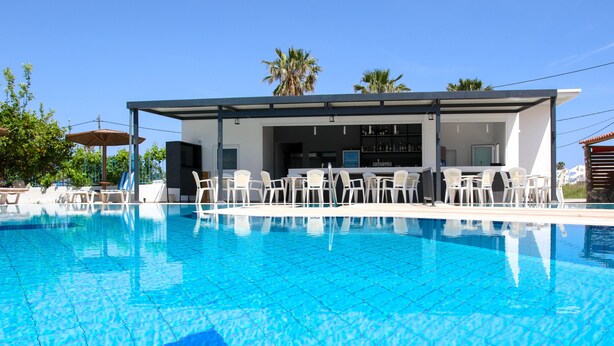 Une piscine entourée de chaises longues blanches et un espace bar équipé d’un téléviseur.