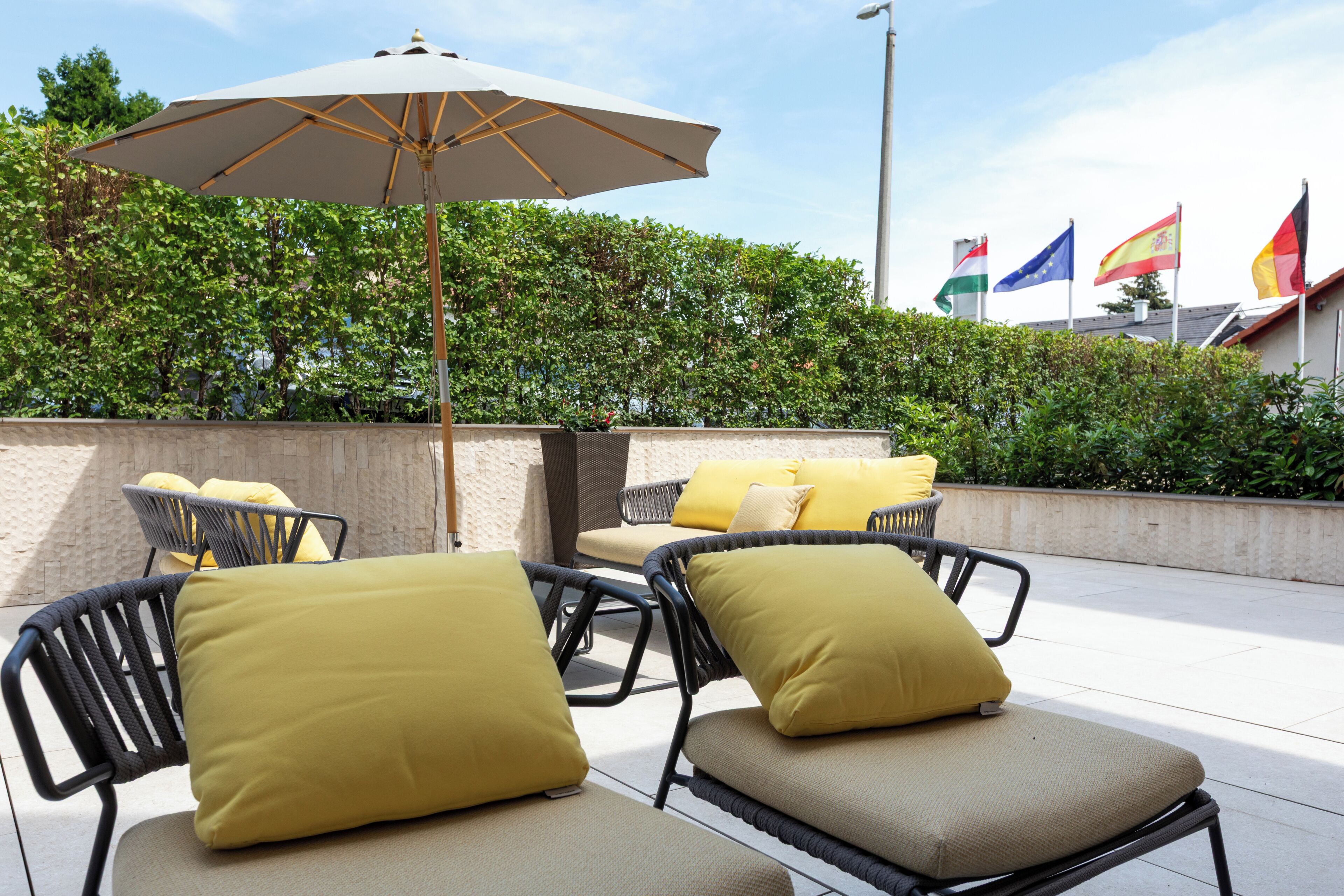 Outdoor seating with yellow cushions, a large umbrella, and flags in the background.