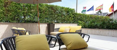 Outdoor seating with yellow cushions, a large umbrella, and flags in the background.