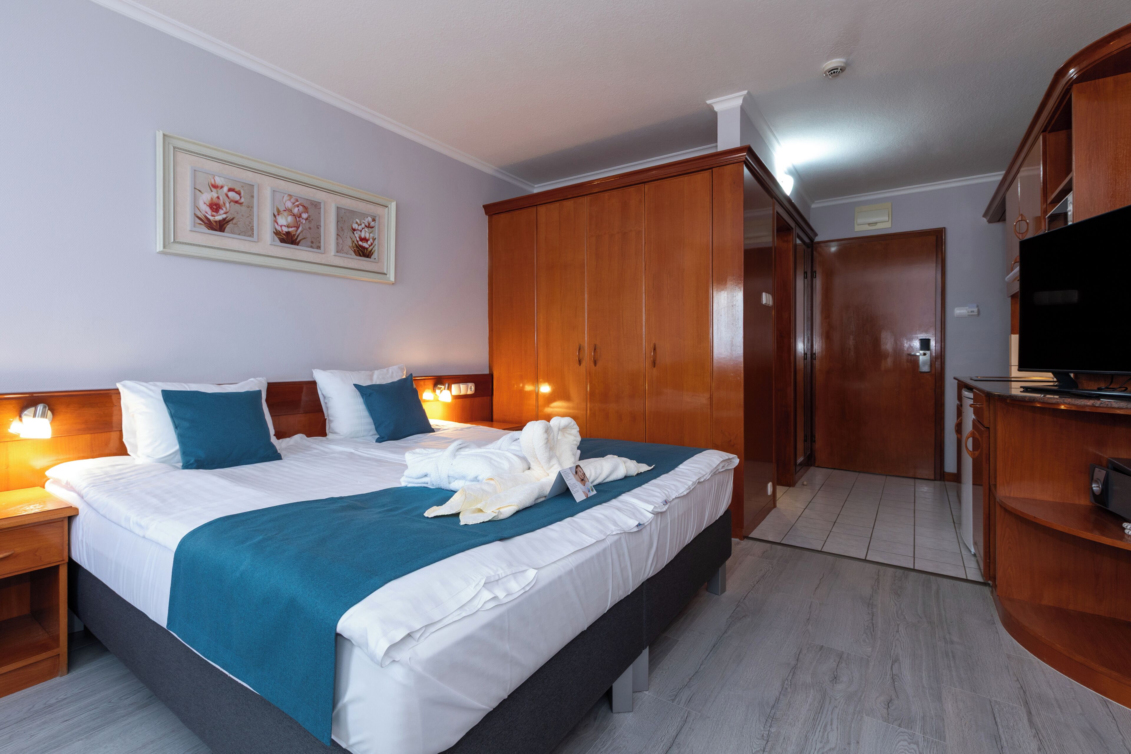 Quarto de hotel com uma cama grande, guarda-roupa de madeira, televisão e uma obra de arte emoldurada na parede.