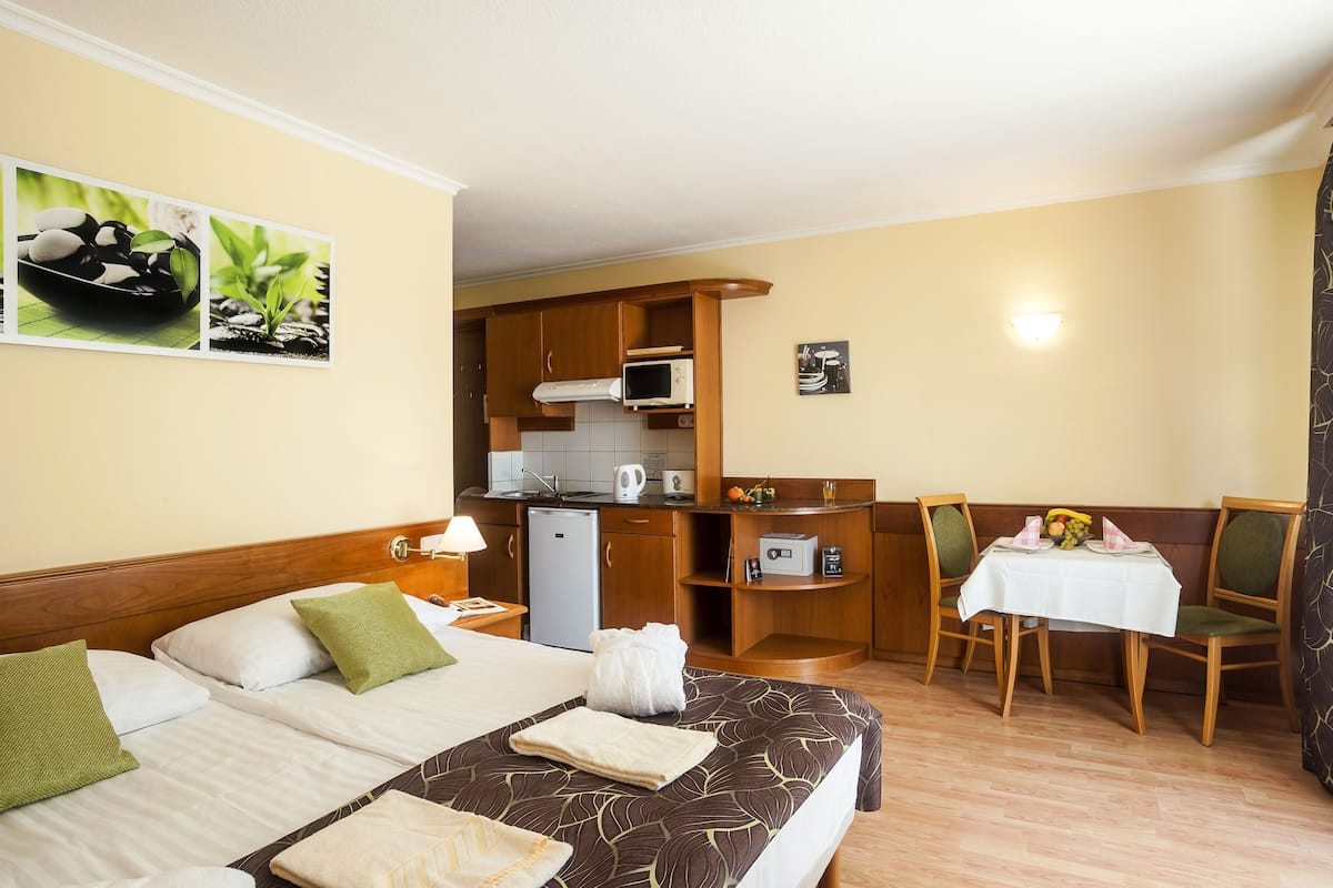 A hotel room with two beds, a kitchenette, a dining area, and a wall-mounted picture.