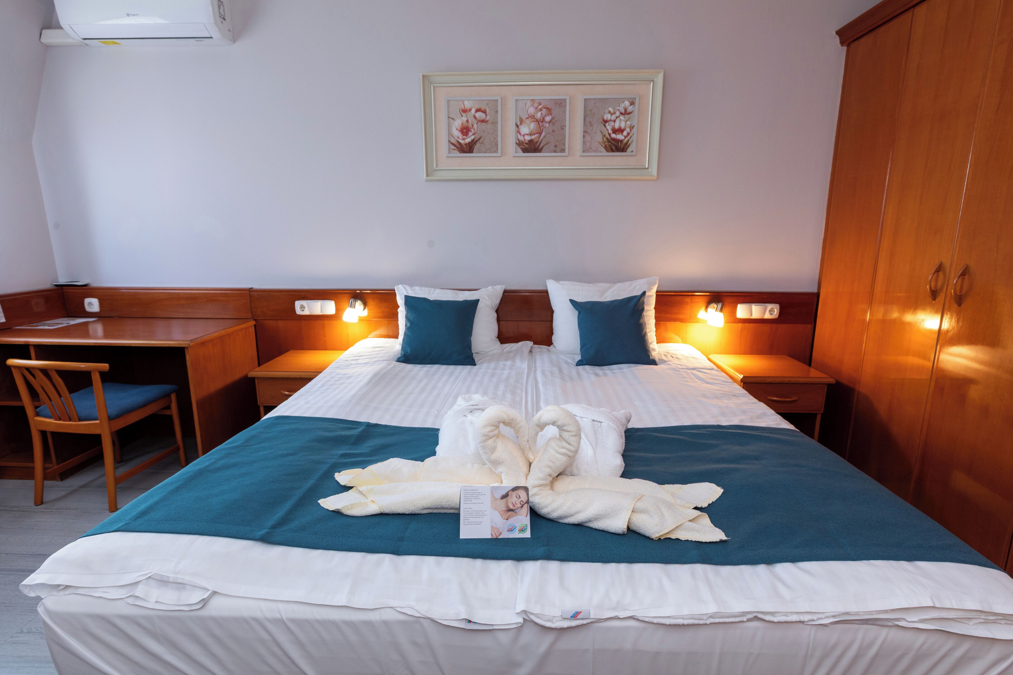 A hotel room with a bed, two bedside tables, a desk, a chair, and a wardrobe.
