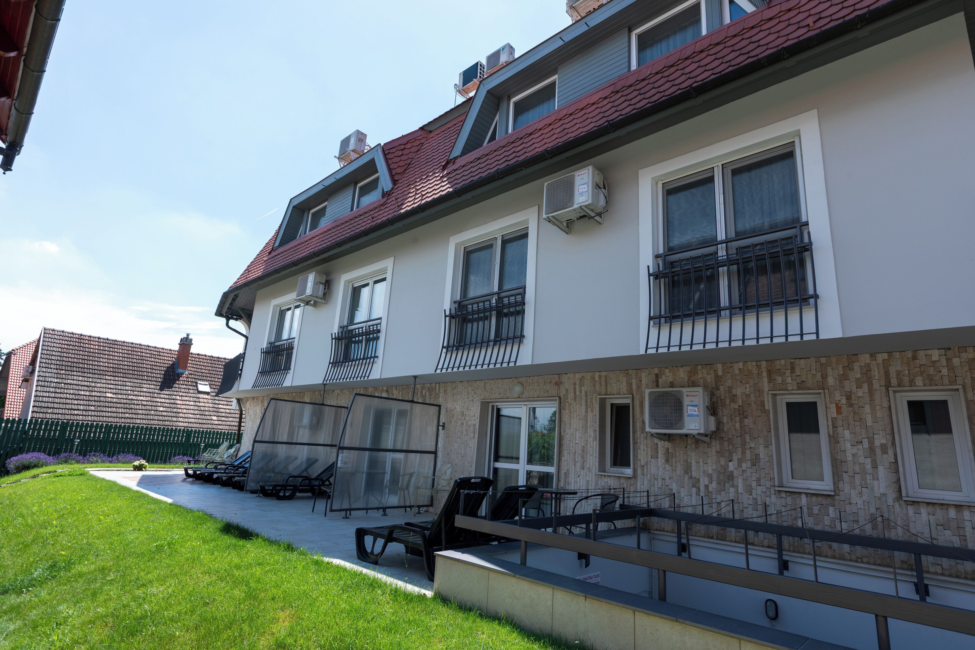 A multi-story building with balconies, outdoor seating, and a paved walkway.