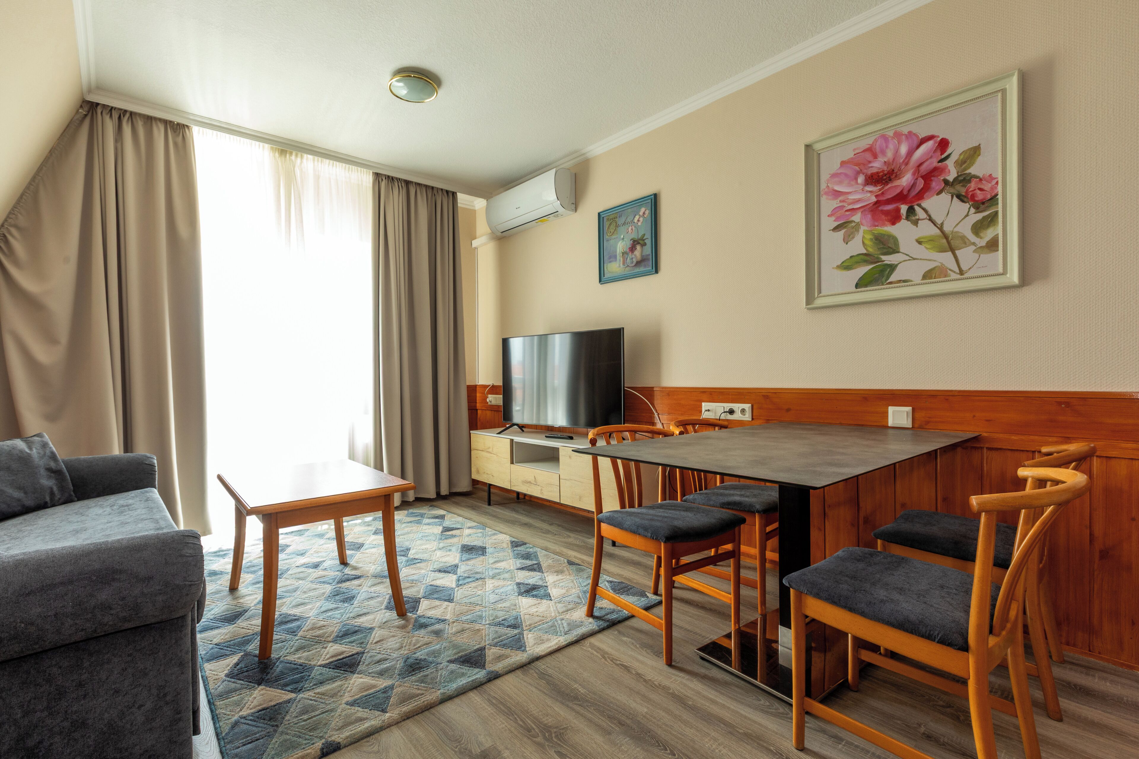 A modern living room with a sofa, a dining table with chairs, a TV, and a painting on the wall.