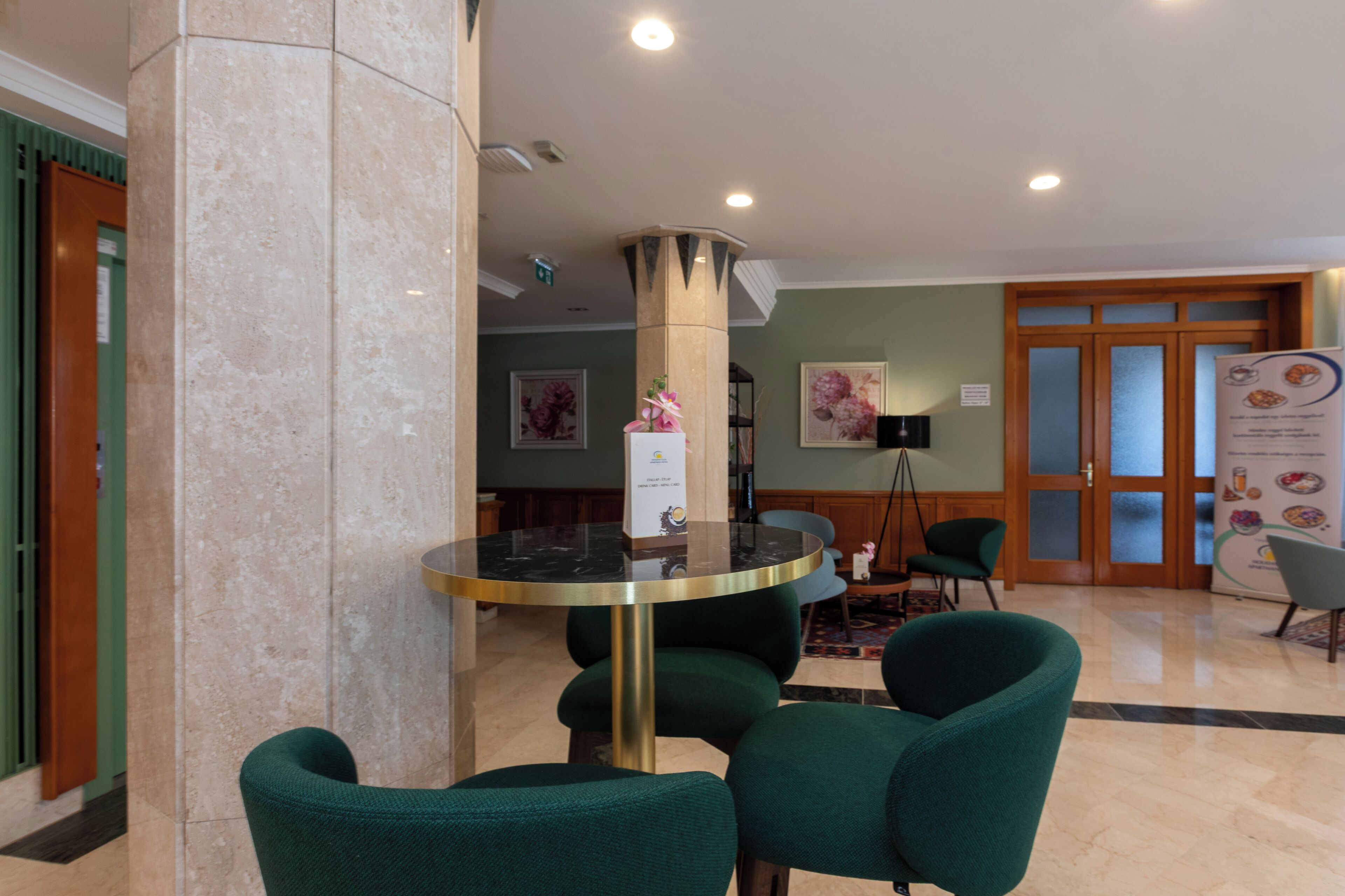 A lobby with a marble column, a glass-top table, and green upholstered chairs.