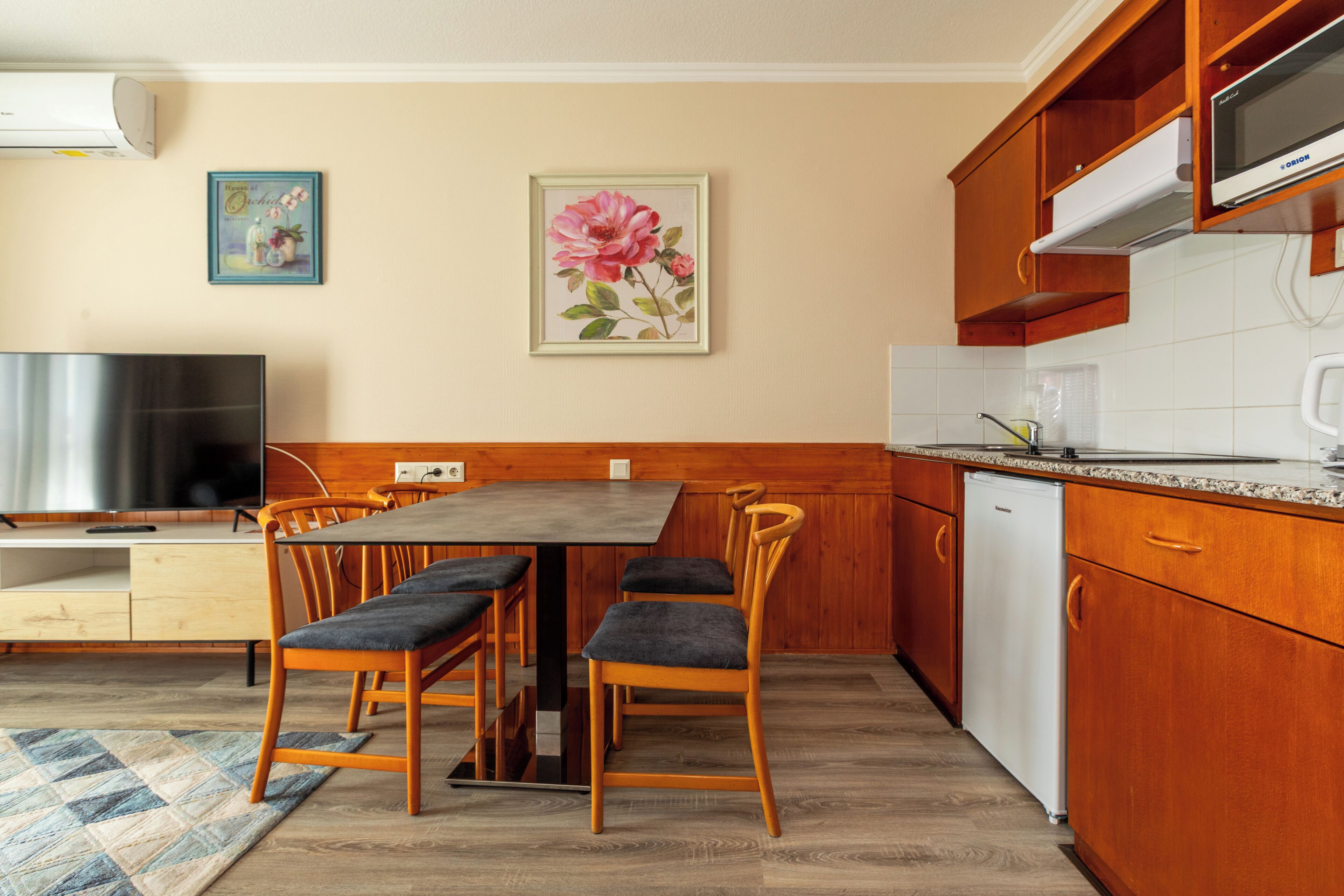Una cucina con mobili in legno, un tavolo da pranzo con sedie, una TV e un frigorifero.