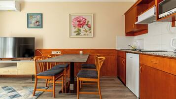 Una cocina con armarios de madera, una mesa de comedor con sillas, un televisor y un refrigerador.