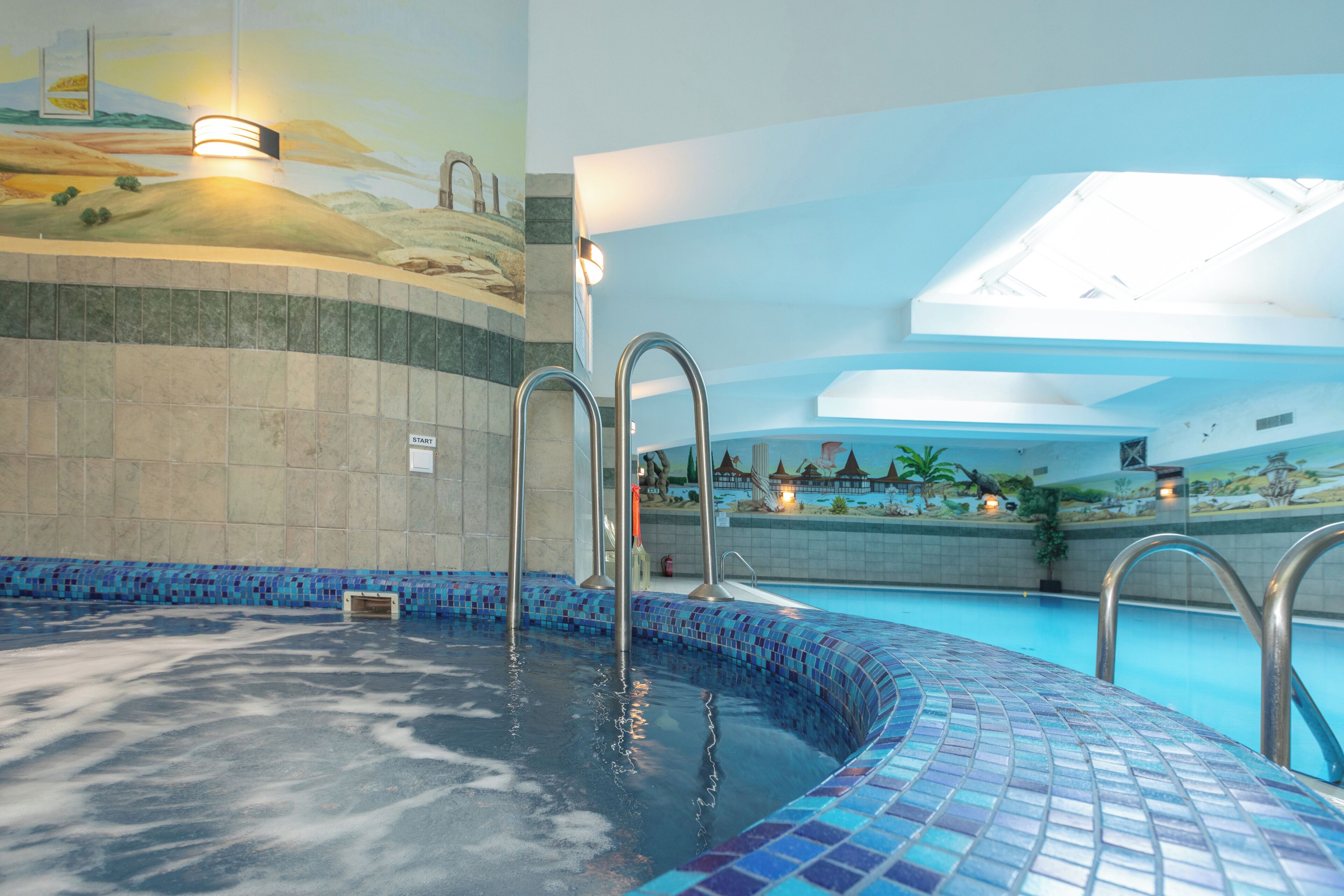 A swimming pool with tiled edges, a mural on the wall, and a 'START' sign.
