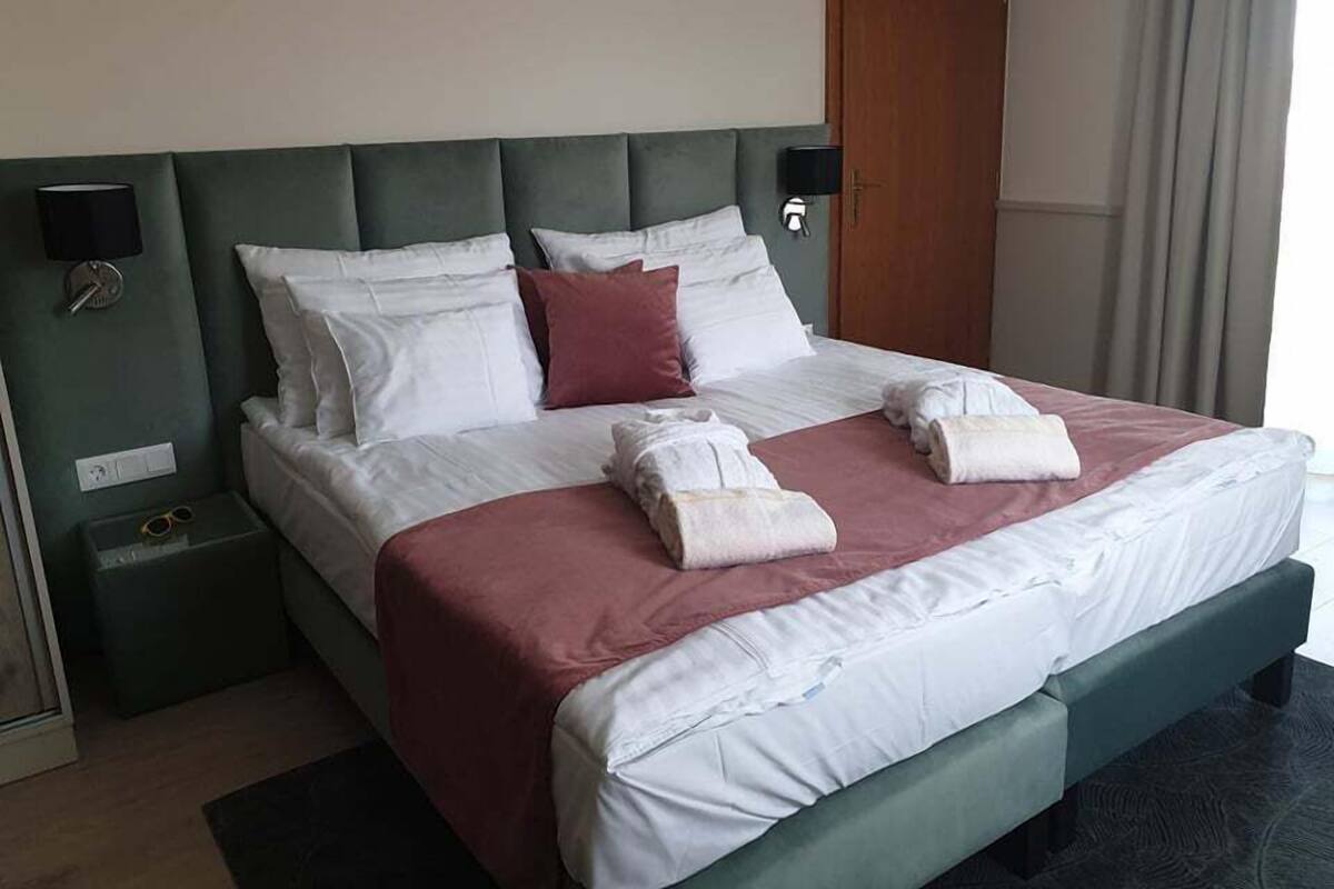 A hotel room with a bed, pillows, a nightstand, a lamp, and a door.