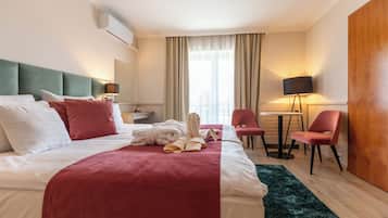 A hotel room with a bed, a desk, a chair, a lamp, and a window with curtains.