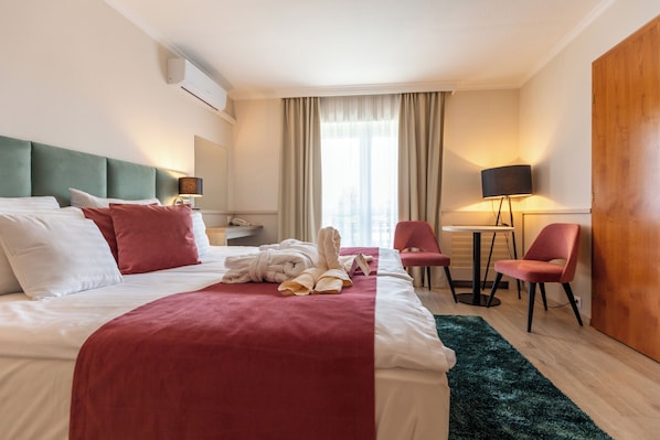 A hotel room with a bed, a desk, a chair, a lamp, and a window with curtains. - Holiday Club Apartman Hotel (Hévíz)