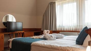 A hotel room with a bed, a desk with a television, a mirror, and a window with curtains.