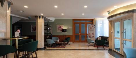 A lobby with a reception desk, green chairs, a coffee bar, and a seating area with sofas and a rug.