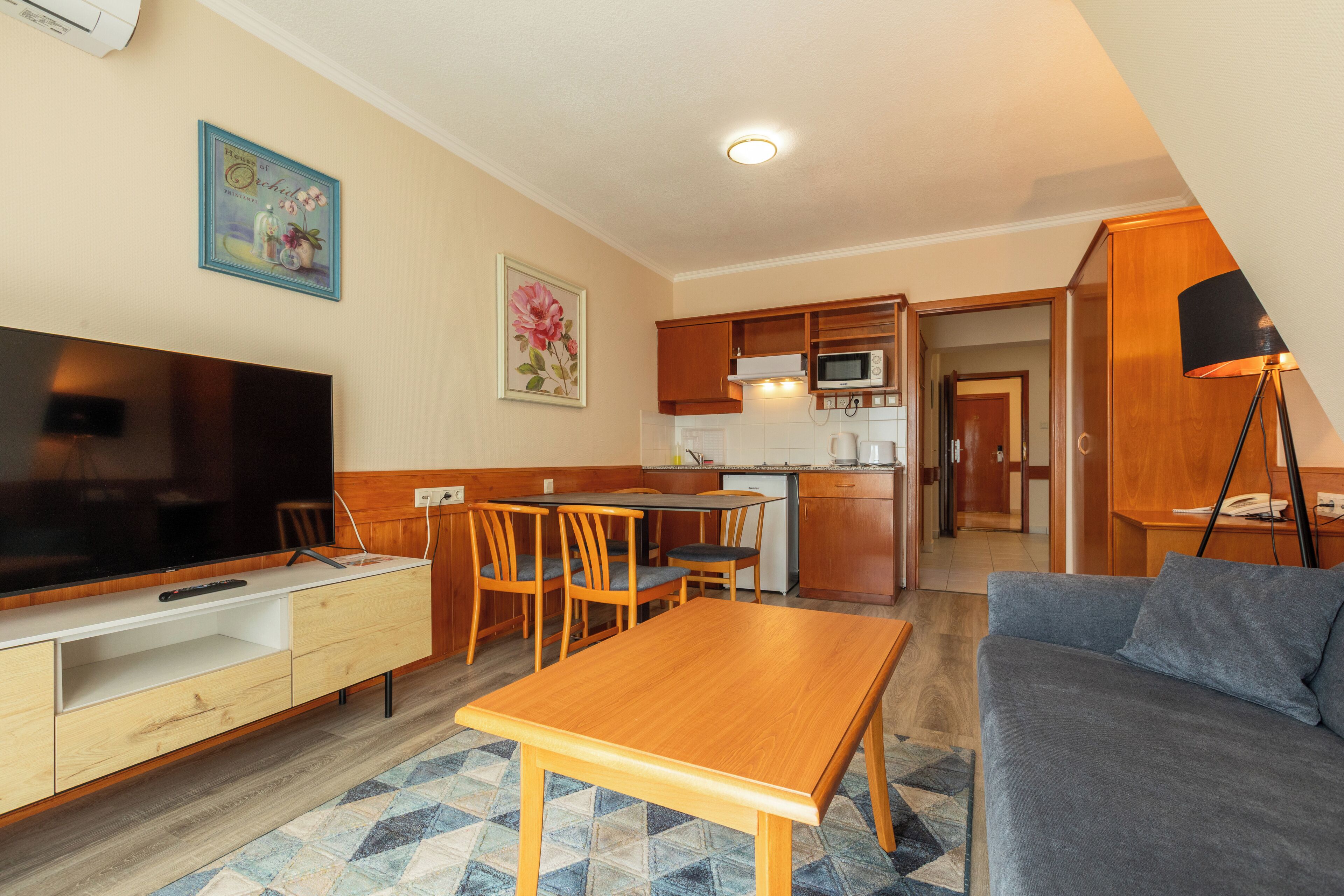 Un espace de vie compact comprenant un téléviseur, des meubles en bois, une kitchenette et un canapé.