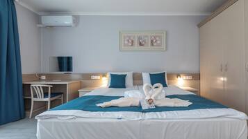 A hotel room with a bed, desk, chair, and a wall-mounted air conditioner.