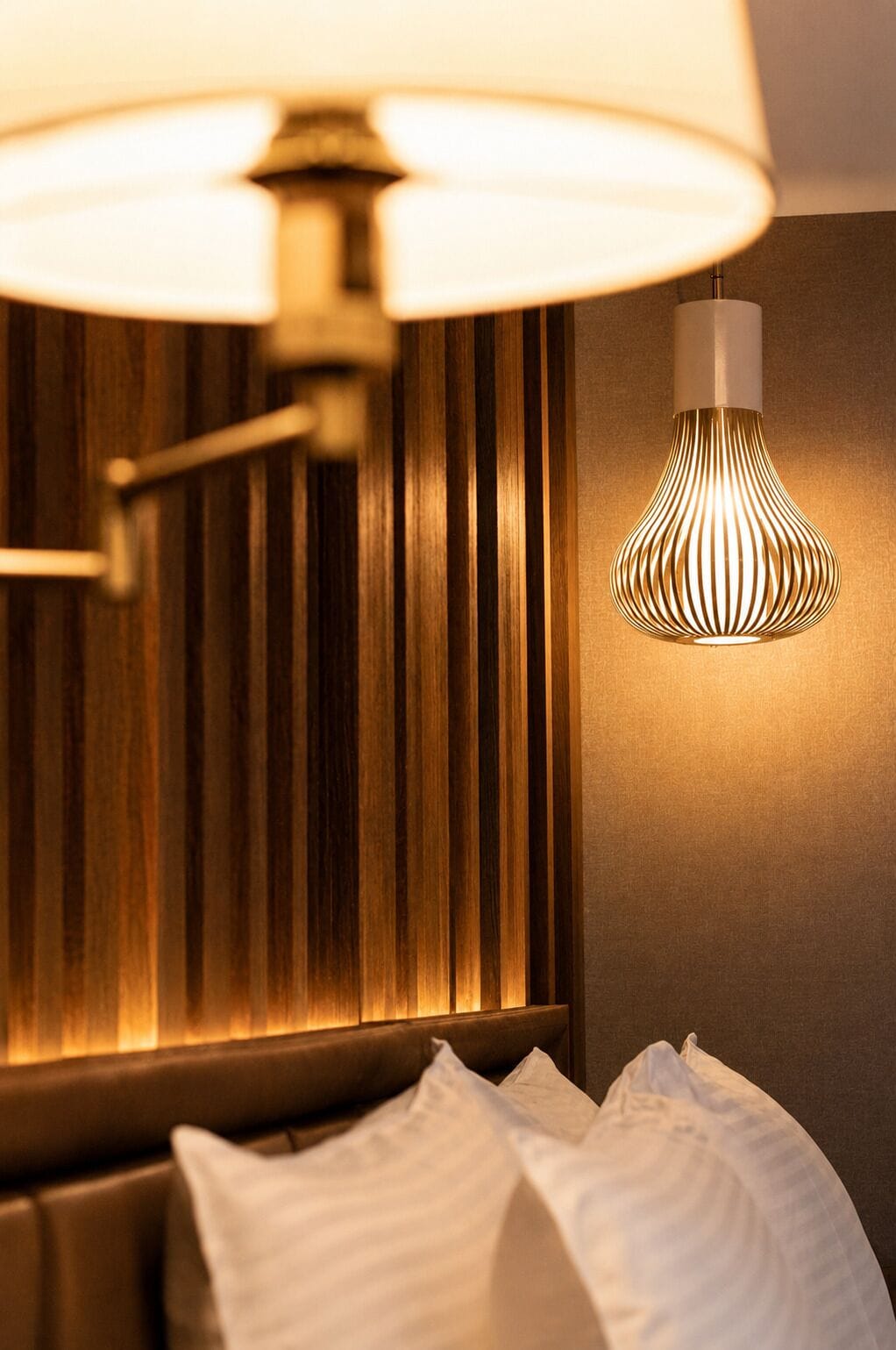 Une chambre d’hôtel avec un lit, une lampe fixée au mur et un luminaire au plafond.
