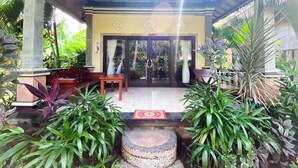 A covered outdoor area with a wooden bench, a table, and potted plants. - Bali Bhuana Beach Cottage (Karangasem)