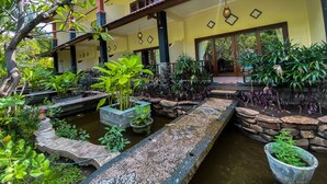 A courtyard with a water feature, potted plants, and a building with a tiled roof and columns. - Bali Bhuana Beach Cottage (Karangasem)