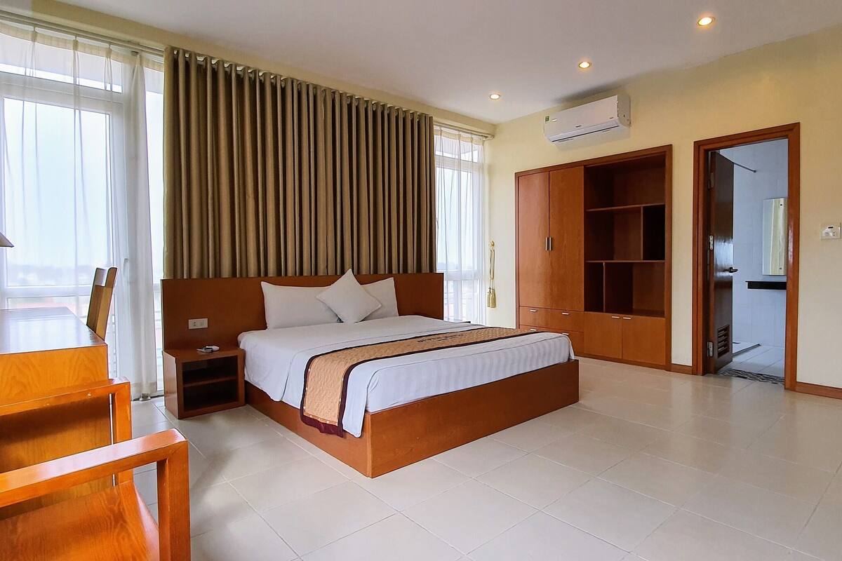 A hotel room with a large bed, a desk, a chair, a wardrobe, and a TV.