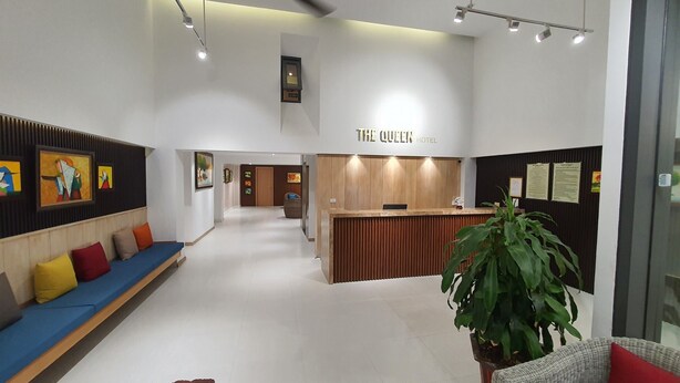 Un hall d’hôtel avec un comptoir d’accueil en bois, un canapé bleu agrémenté de coussins colorés et des œuvres d’art encadrées accrochées aux murs.