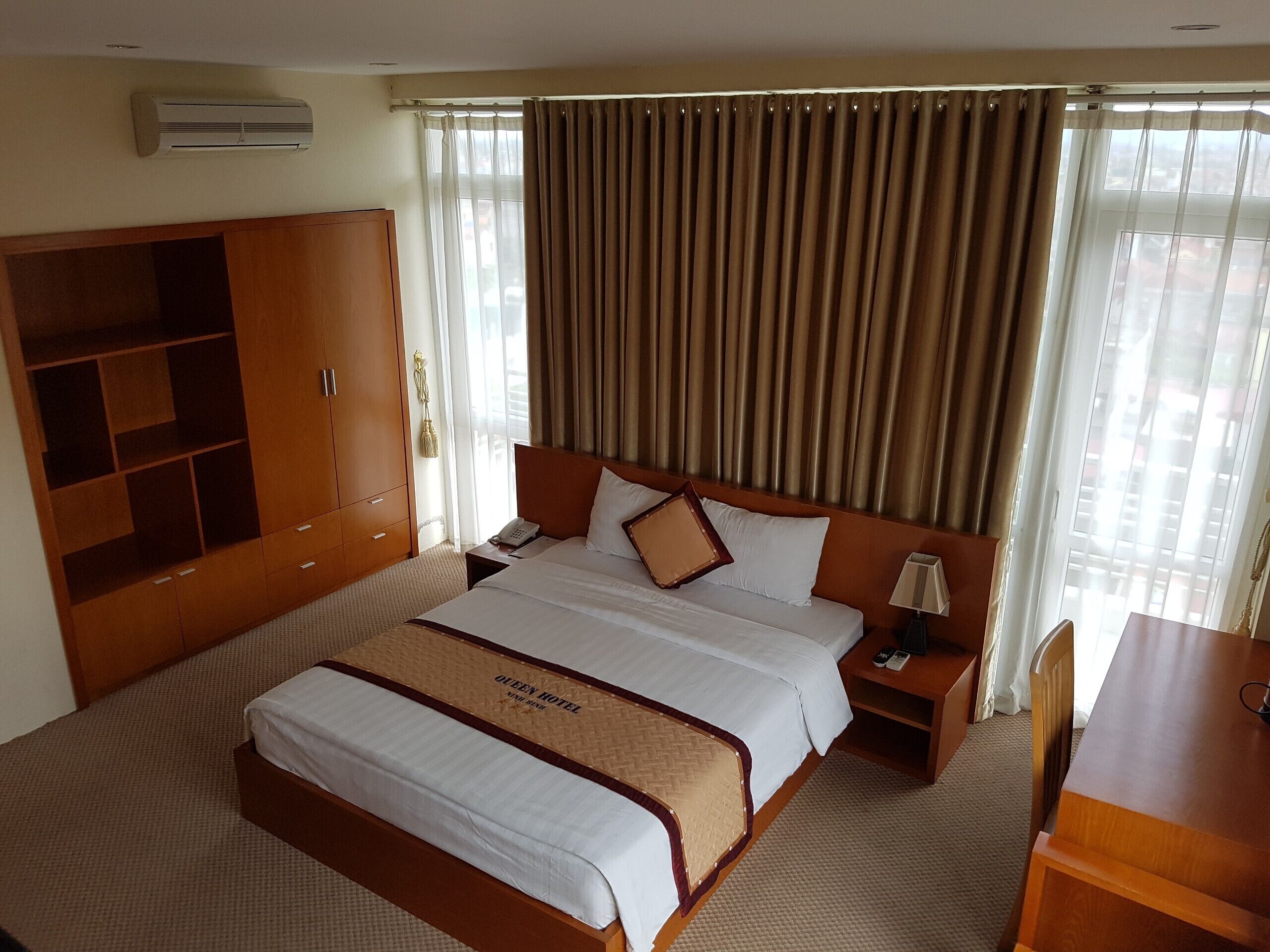 Habitación de hotel con una cama grande, un armario, una mesita de noche con lámpara y vistas al exterior a través de la ventana.