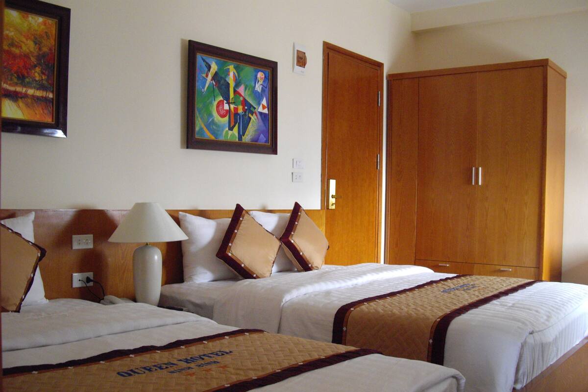 A hotel room with two beds, a nightstand, a lamp, a painting, and a wardrobe.